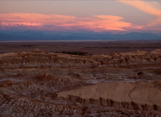 Desert landscape at sunset with pink clouds over distant mountains