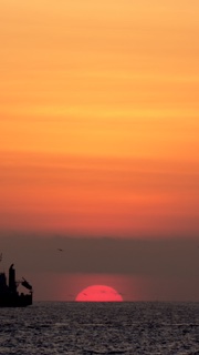 Red sun setting into the sea under an orange sky