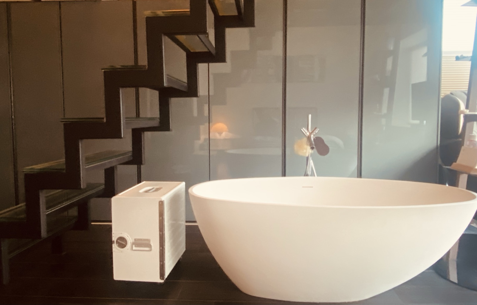 Freestanding sculptural bathtub beneath a floating black steel staircase